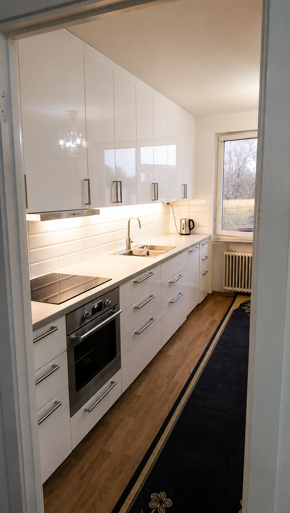 Kök efter renovering med vita högskåp, ny bänkskiva och inbyggd belysning.