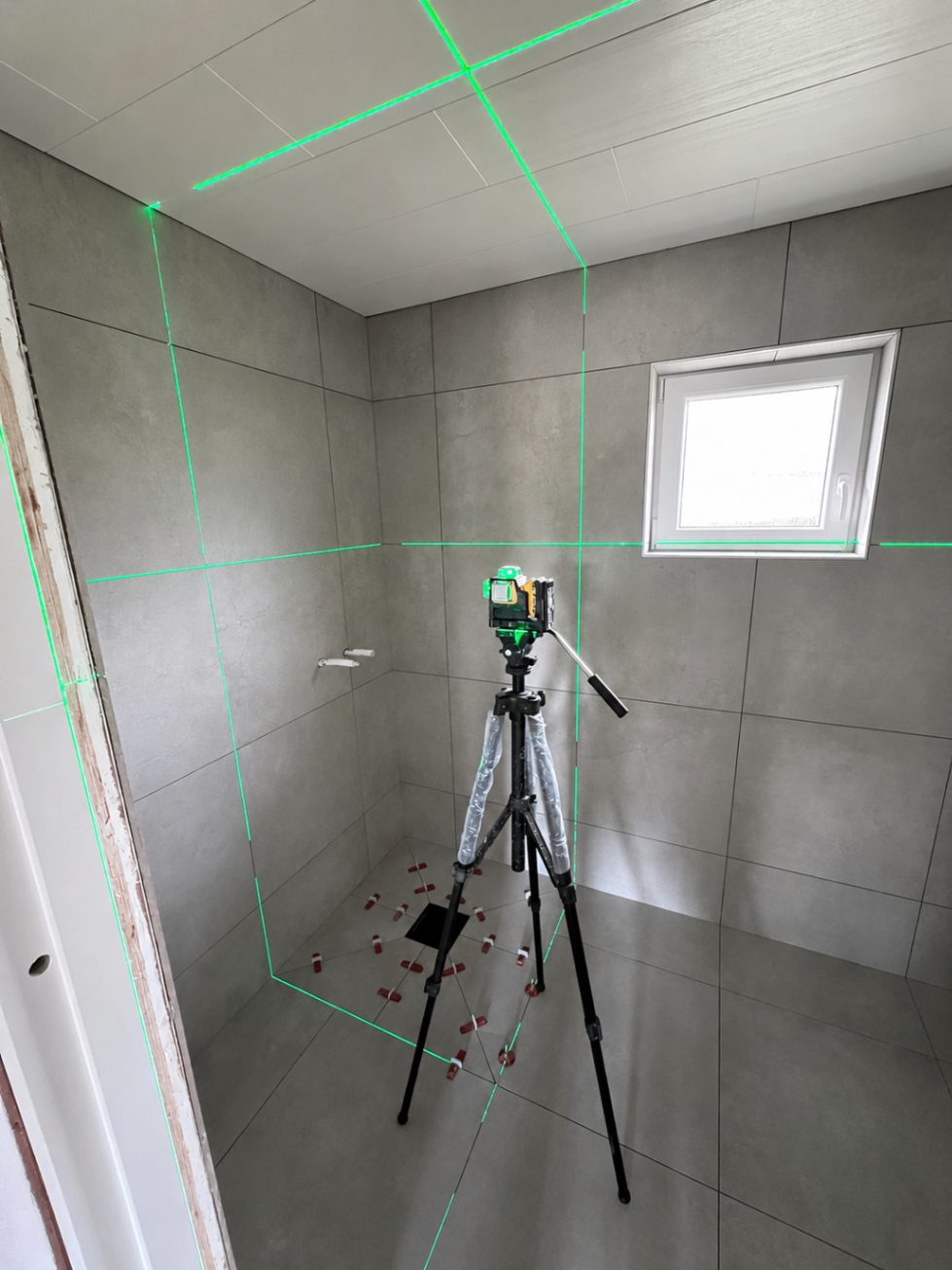 Badrum under plattsättning med laserlinjer för millimeterprecision.